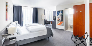 Helles Hotelzimmer mit Doppelbett, Sitzbereich, Kunstwerken und Zugang zu einem Badezimmer im ATLANTIC Hotel Vegesack.