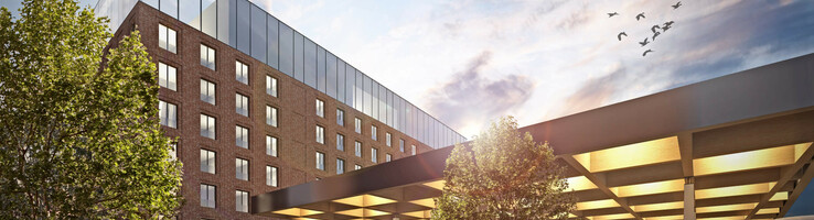 uniq by ATLANTIC Hotels in Kiel Modernes Hotel mit Glasfassade, Menschen im Eingangsbereich, Bäume und Himmel mit Vögeln im Hintergrund.