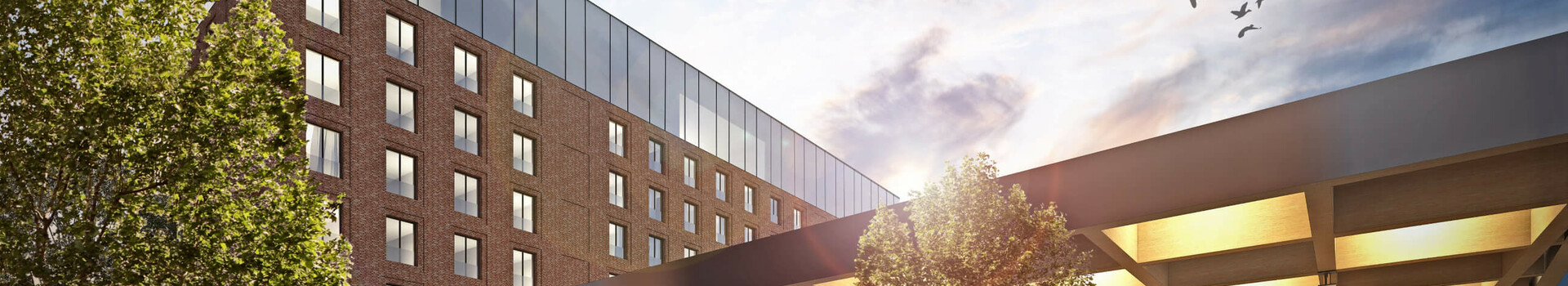 uniq by ATLANTIC Hotels in Kiel Modernes Hotel mit Glasfassade, Menschen im Eingangsbereich, Bäume und Himmel mit Vögeln im Hintergrund.