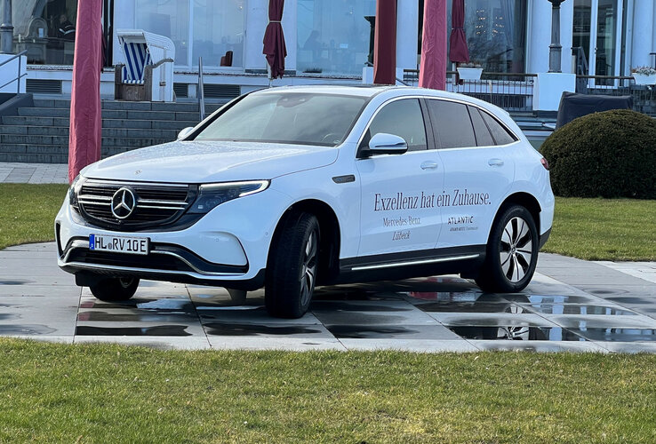 Weißes Elektroauto vor dem ATLANTIC Grand Hotel Travemünde, mit Schriftzug "Exzellenz hat ein Zuhause".
