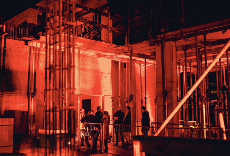 Baustelle des ATLANTIC Hotel Münster bei Nacht, rot beleuchtet, mit Personen in Schutzkleidung.