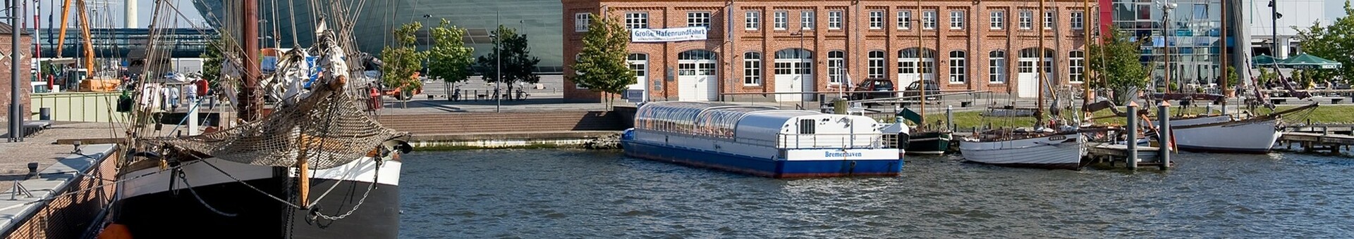 ATLANTIC Hotel Sail City in Bremerhaven, modernes Hochhaus am Wasser mit Segelschiff im Vordergrund.