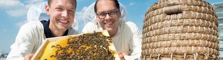 Two beekeepers in protective clothing present a honeycomb on the roof of the ATLANTIC Hotel Sail City.