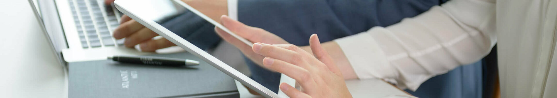 Different media with ATLANTIC Hotels Two people working on a laptop and tablet in a modern hotel environment, with a notebook and glass of water on the table.