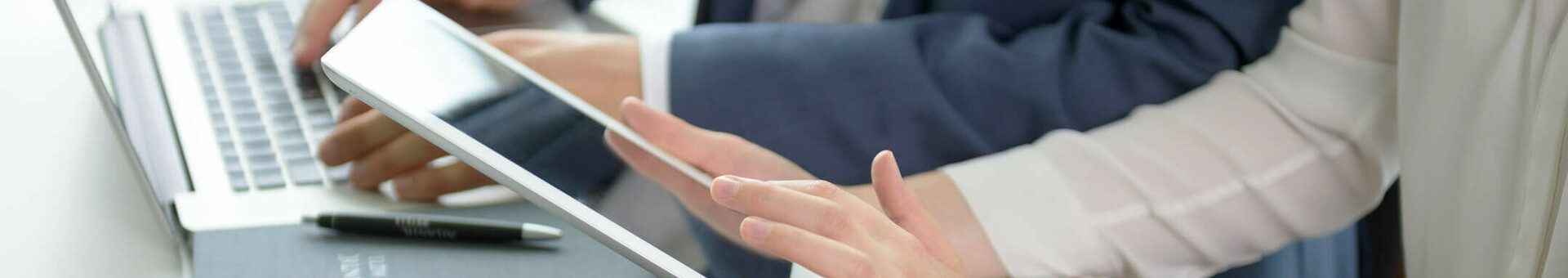 Smarte Media-Nutzung in den ATLANTIC Hotels Zwei Personen arbeiten an Laptop und Tablet in moderner Hotelumgebung, mit Notizbuch und Wasserglas auf dem Tisch.