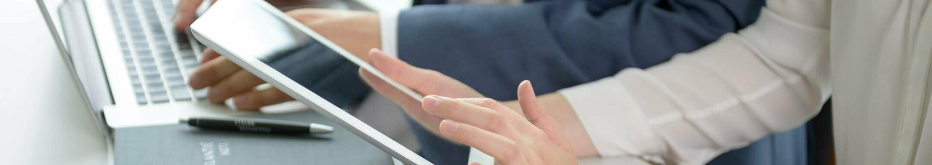 Two people working on a laptop and tablet in a modern hotel environment, with a notebook and glass of water on the table.