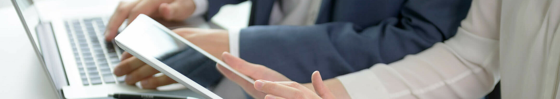 Zwei Personen arbeiten an Laptop und Tablet in moderner Hotelumgebung, mit Notizbuch und Wasserglas auf dem Tisch.