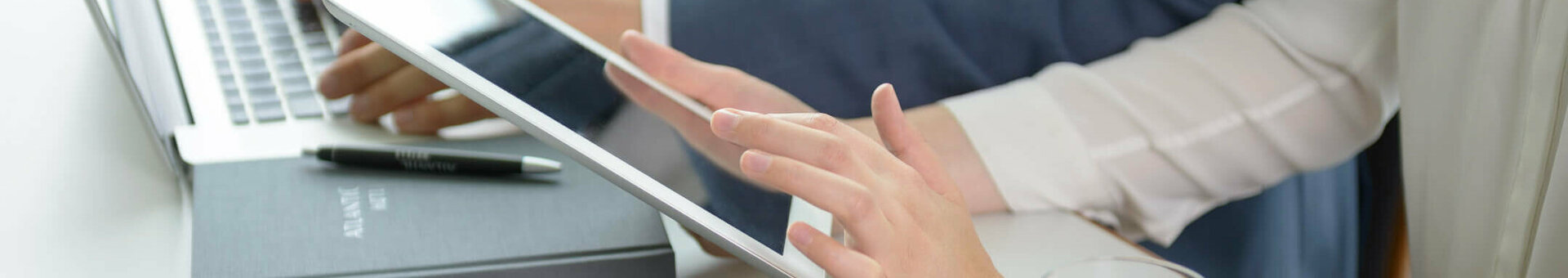 Different media with ATLANTIC Hotels Two people working on a laptop and tablet in a modern hotel environment, with a notebook and glass of water on the table.