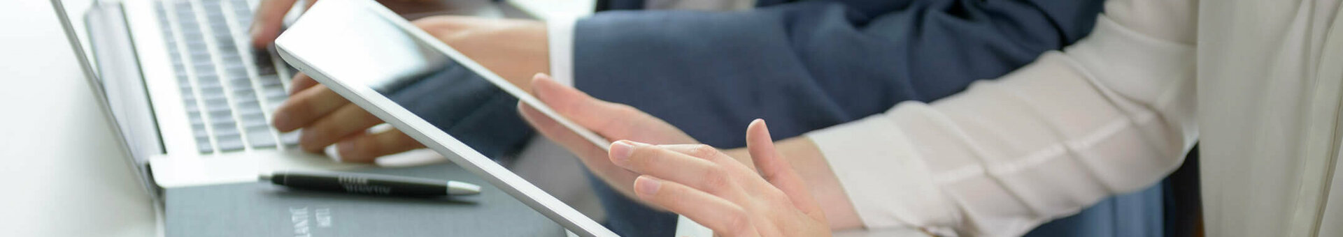 Different media with ATLANTIC Hotels Two people working on a laptop and tablet in a modern hotel environment, with a notebook and glass of water on the table.