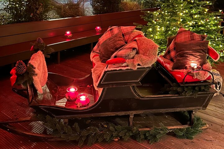 Gemütlich dekorierter Schlitten mit Kissen und Decken, umgeben von Kerzenlichtern und einem beleuchteten Weihnachtsbaum.