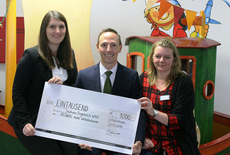 Drei Personen halten einen symbolischen Scheck über 1000 Euro im ATLANTIC Hotel Wilhelmshaven.