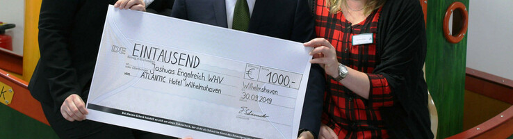 Drei Personen halten einen symbolischen Scheck über 1000 Euro im ATLANTIC Hotel Wilhelmshaven.