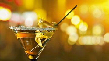 ATLANTIC Grand Hotel Travemünde Cocktail in der Happy Hour Cocktailglas mit Zuckerrand und Zitronenschale vor unscharfem, warm beleuchtetem Hintergrund im ATLANTIC Grand Hotel.