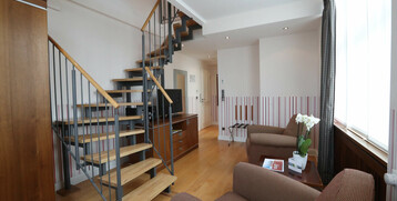 Hotelzimmer mit moderner Holztreppe, gemütlichen Sesseln, TV und Fenster mit Vorhängen im ATLANTIC Grand Hotel Travemünde.