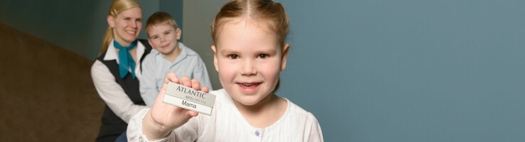 Little girl wearing a night gown is holding up a sign saying "Mama" in the ATLANTIC Hotel SAIL City – The family-friendly workplace
