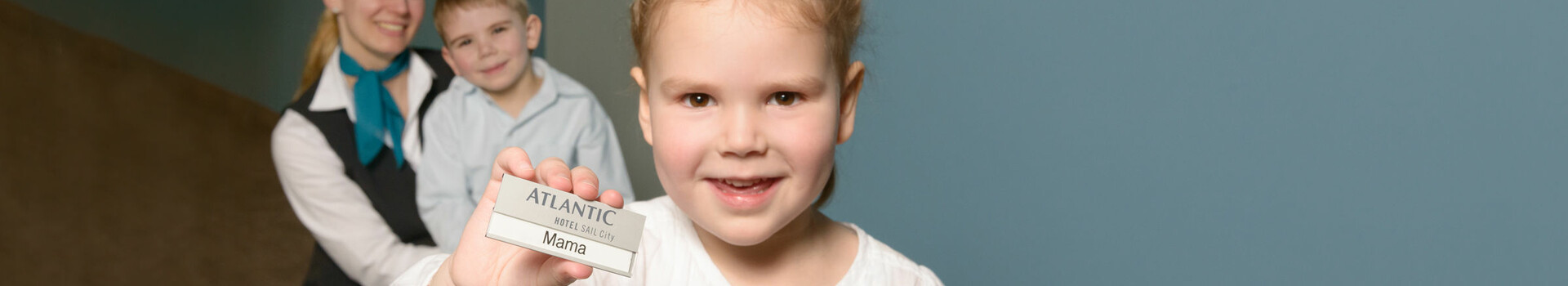 Little girl wearing a night gown is holding up a sign saying "Mama" in the ATLANTIC Hotel SAIL City – The family-friendly workplace