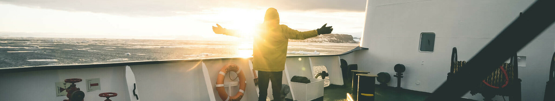 Project Antarctica | Film Person standing on a ship, arms outstretched as the sun sets over the sea.