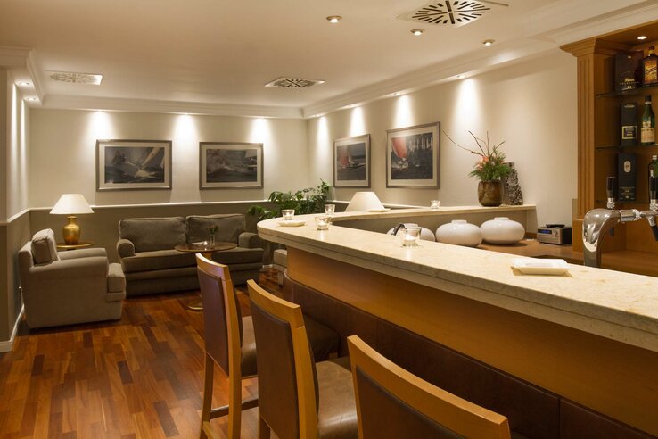 Gemütliche Hotelbar mit Holzboden, Sitzbereich, Theke und dekorativen Bildern an der Wand.