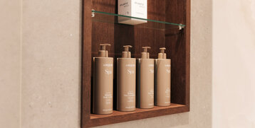 Holzregal mit Pflegeprodukten und einer Komfortbox im ATLANTIC Hotel Heidelberg Badezimmer.