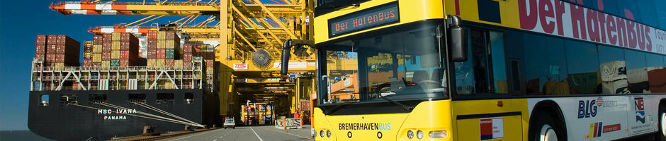 Yellow double-decker bus in the port of Bremerhaven in front of a container ship and cranes under a clear sky.