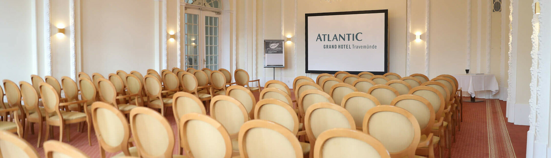 conference room "Bremen" Elegant conference room with chandeliers, rows of chairs and a screen at the ATLANTIC Grand Hotel Travemünde.