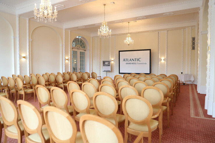 Eleganter Konferenzraum mit Kronleuchtern, Reihen von Stühlen und einer Leinwand im ATLANTIC Grand Hotel Travemünde.