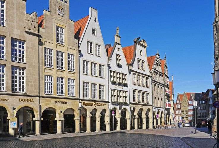 Historic row of houses with arcades and red roofs on Prinzipalmarkt in Münster under a blue sky.