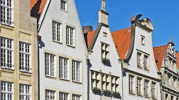 Historische Häuserzeile mit Arkaden und roten Dächern am Prinzipalmarkt in Münster bei blauem Himmel.