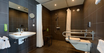 Barrier-free bathroom with shower, grab rails, washbasin and WC in the ATLANTIC Hotel Sail City, Bremerhaven.
