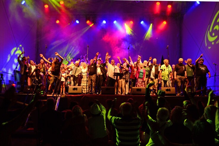 A large group of people celebrate on a colorfully lit stage in front of a cheering audience.