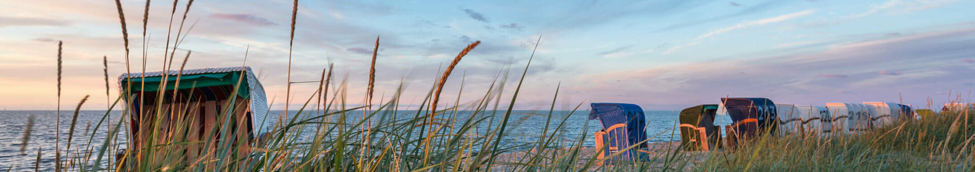 ATLANTIC Hotel Wilhelmshaven | Beach chair Beach chairs by the sea at sunset, surrounded by tall grass under a blue sky.