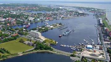 Luftaufnahme des ATLANTIC Hotel Wilhelmshaven am Wasser mit umliegendem Hafen und Stadtansicht.