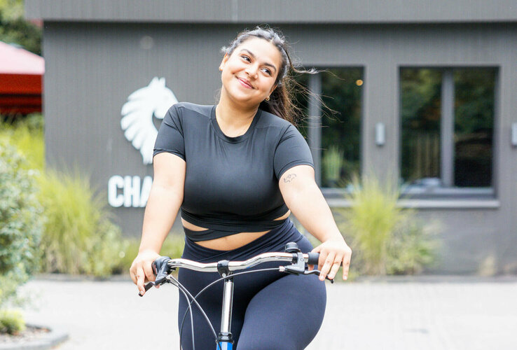 Frau auf blauem Fahrrad vor dem ATLANTIC Hotel Landgut Horn Bremen, lächelnd und entspannt.