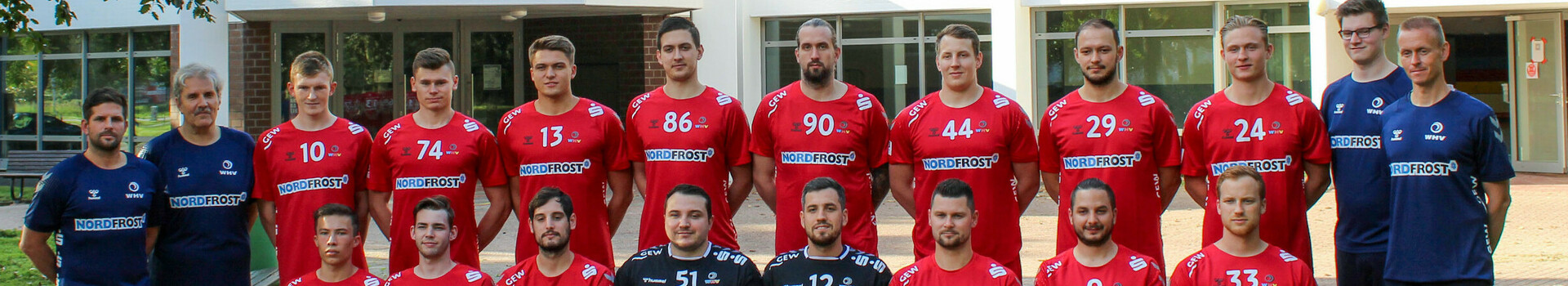 Sponsoring Wilhelmshavener Handball Verein | ATLANTIC Hotel Wilhelmshaven Eine Handballmannschaft in roten Trikots posiert vor einem Gebäude für ein Gruppenfoto.
