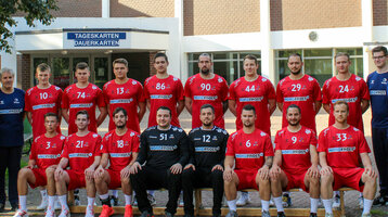 A handball team in red jerseys poses in front of a building for a group photo.