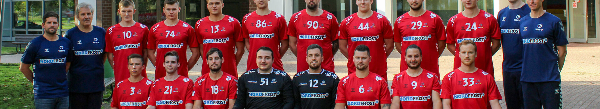 Sponsoring Wilhelmshaven handball club | ATLANTIC Hotel Wilhelmshaven A handball team in red jerseys poses in front of a building for a group photo.
