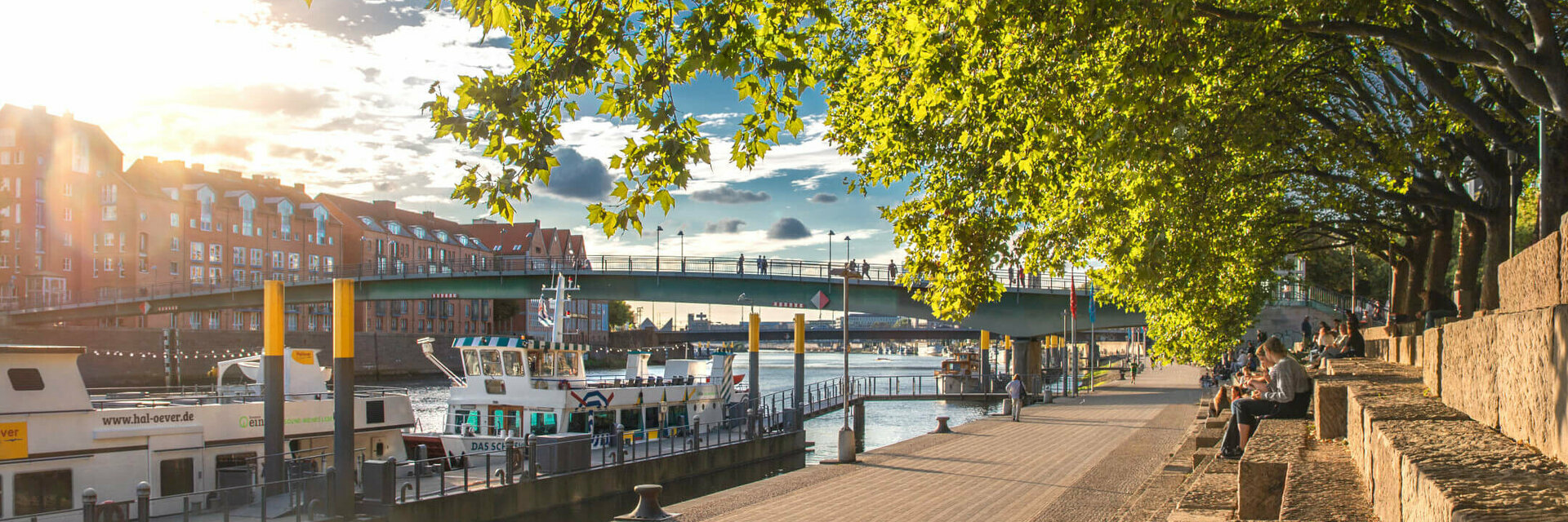 Sunny walk along the Weser with a view of boats, bridge and trees, close to the ATLANTIC Grand Hotel Bremen.