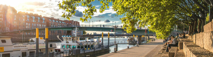 Sunny walk along the Weser with a view of boats, bridge and trees, close to the ATLANTIC Grand Hotel Bremen.