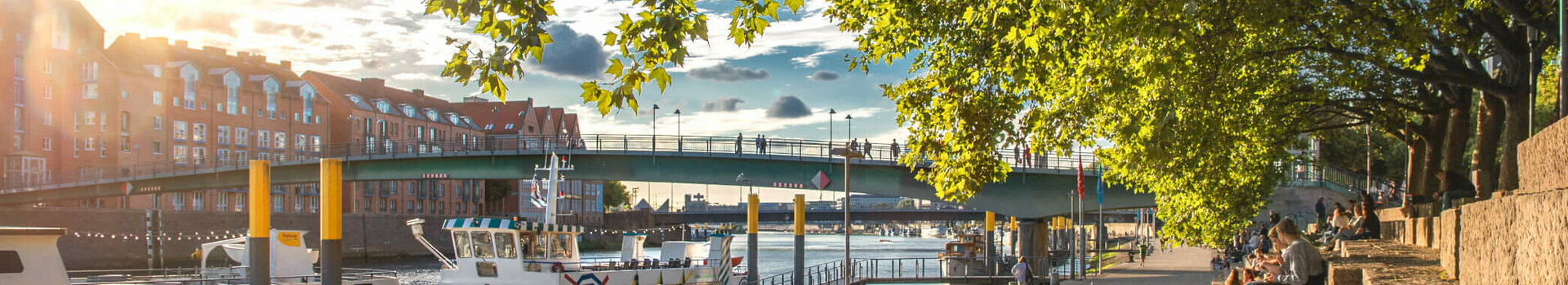 Sunny walk along the Weser with a view of boats, bridge and trees, close to the ATLANTIC Grand Hotel Bremen.