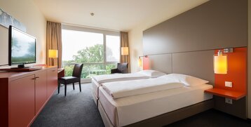 Bright hotel room with double bed, large window, TV, desk and modern furnishings at the ATLANTIC Hotel Galopprennbahn.