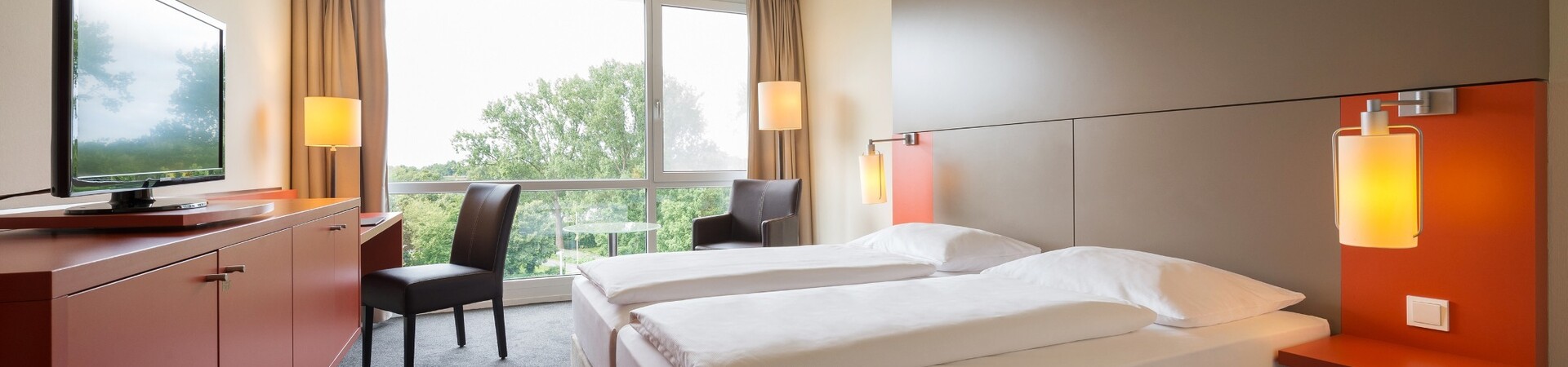 Interior view of the Double Room in the ATLANTIC Hotel Galopprennbahn  Bright hotel room with double bed, large window, TV, desk and modern furnishings at the ATLANTIC Hotel Galopprennbahn.