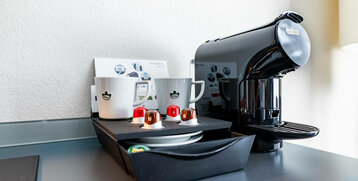 Kaffeemaschine mit Tassen und Kapseln auf einem Tisch im ATLANTIC Hotel Vegesack, Bremen.