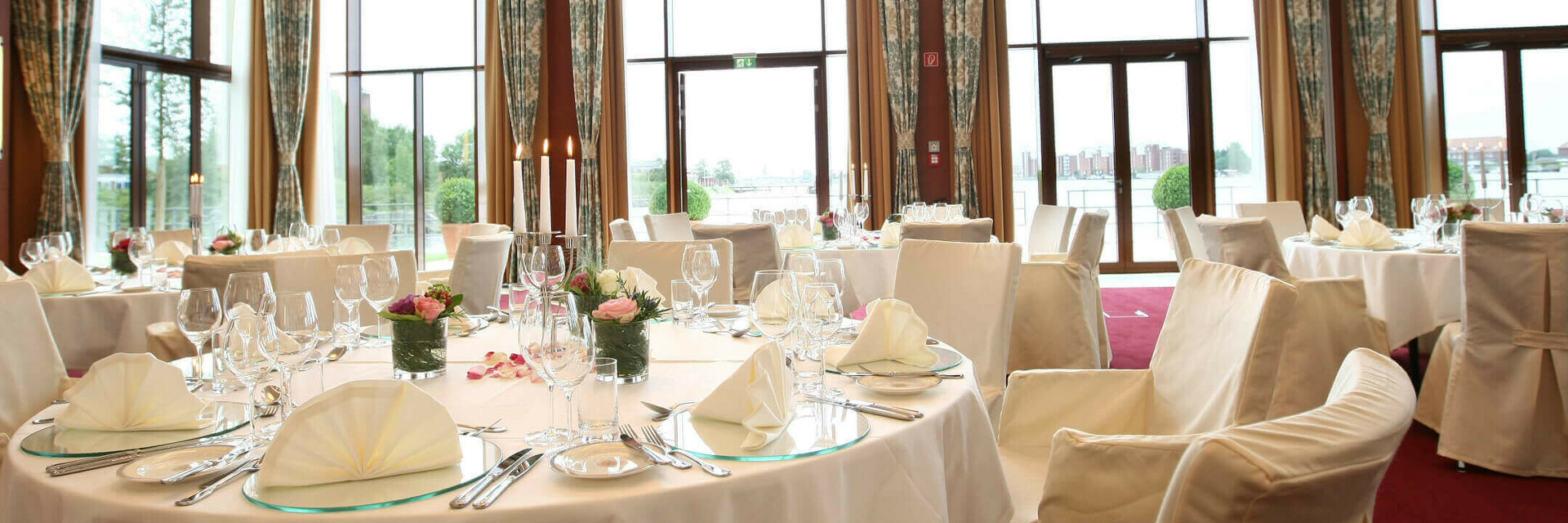 Eleganter Bankettsaal im ATLANTIC Hotel Wilhelmshaven, festlich gedeckte Tische mit Blick auf große Fenster und Wasser.
