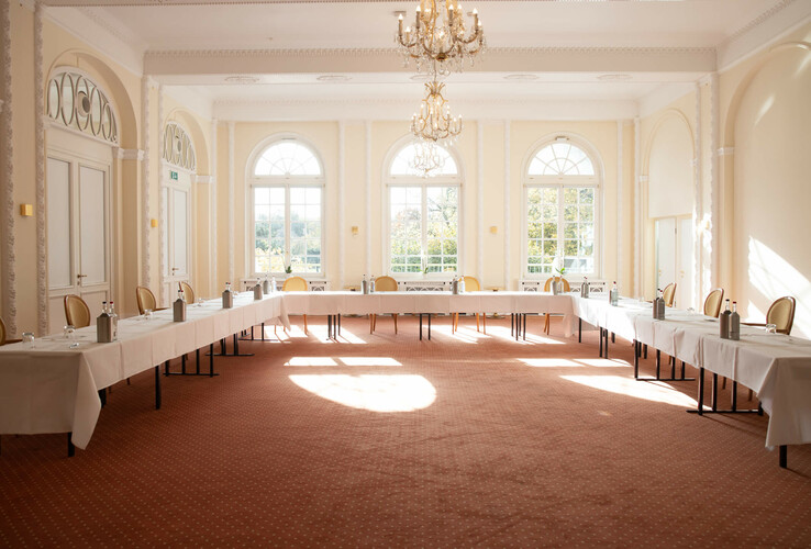 Heller Konferenzraum mit U-förmiger Tischanordnung, großen Fenstern und Kronleuchtern im ATLANTIC Grand Hotel Travemünde.