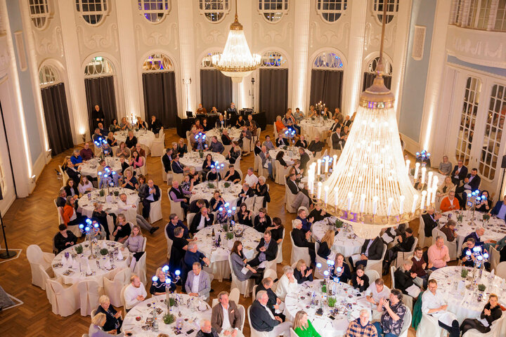 Eleganter Festsaal im ATLANTIC Grand Hotel Travemünde, gefüllt mit Gästen an runden Tischen unter einem großen Kronleuchter.