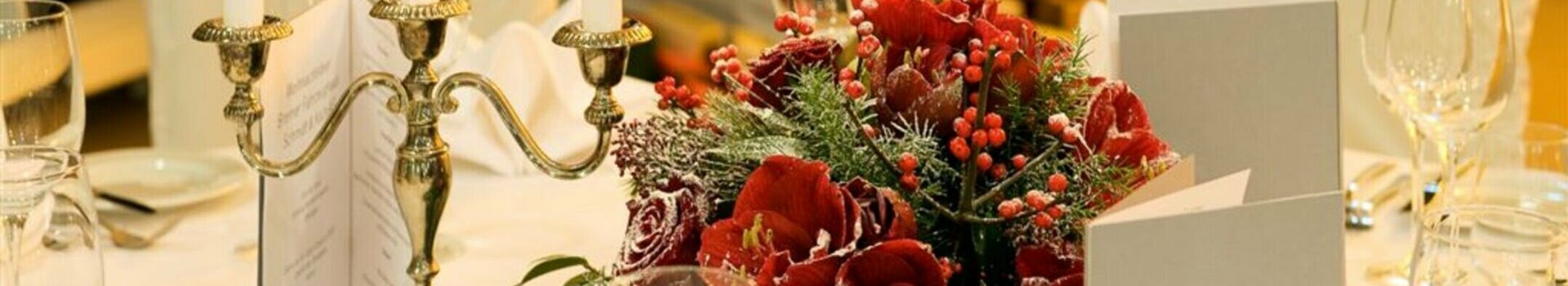 Festively laid table with candlesticks, red flowers and Christmas tree in the background.