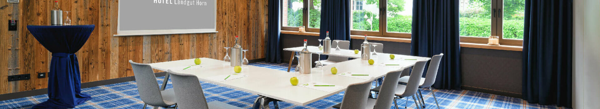 Moderner Konferenzraum im ATLANTIC Hotel Landgut Horn mit Holzwand, blauen Vorhängen und gedecktem Tisch.