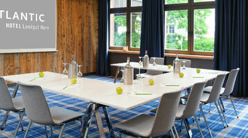 Moderner Konferenzraum im ATLANTIC Hotel Landgut Horn mit Holzwand, blauen Vorhängen und gedecktem Tisch.