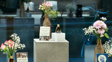 Fünf Aufsteller in Betonoptik, darauf jeweils ein kleiner Blumenstrauß und die Ausstellungsstücke, wie Kaffeebohnen, Duftstäbchen und eine Cocktailprobe.