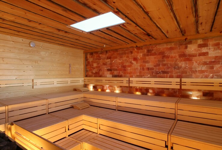 Helle Sauna mit Holzbänken, einem Salzwand-Element und Deckenbeleuchtung.